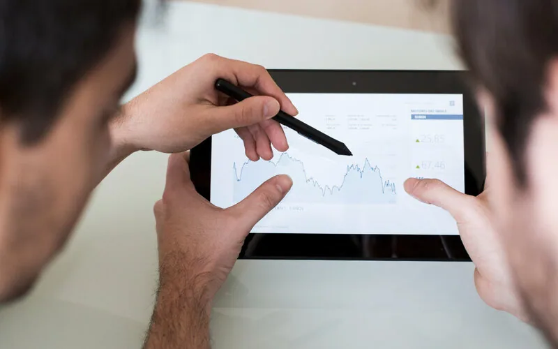 Two people analyzing stock chart on tablet with focused attention
